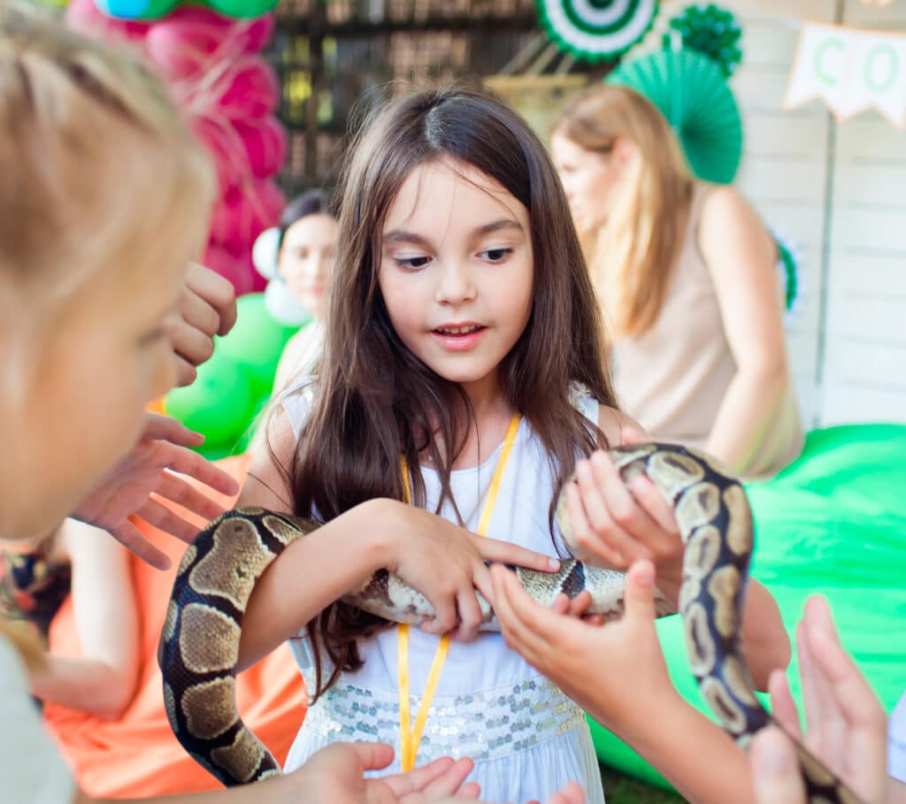 A young, dark-haired girl is holding a long Python snake in her arms.