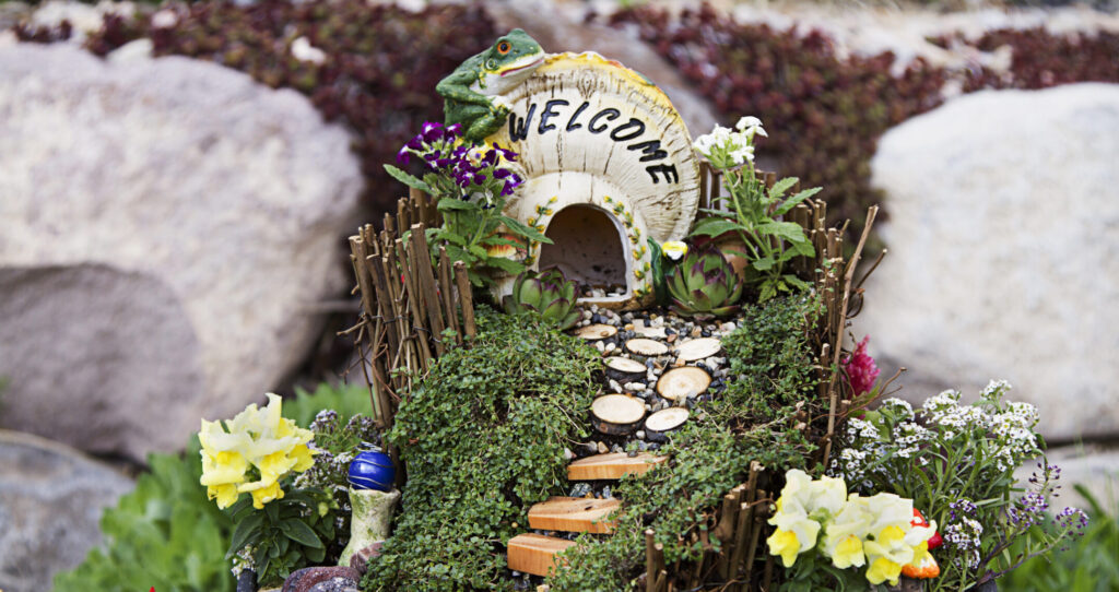 A fantasy toad house with tiny garden path surrounded by plants. The toad house says "welcome" on it.