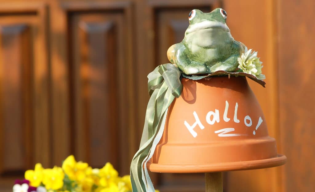 A small flowerpot is hanging upside down. It is being supported by a thick wooden pole and it's decorated with a frog on top.