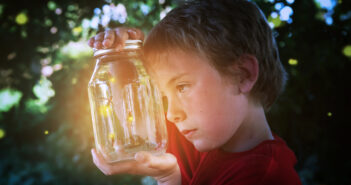 Several fireflies in a jar, with young boy looking at them.